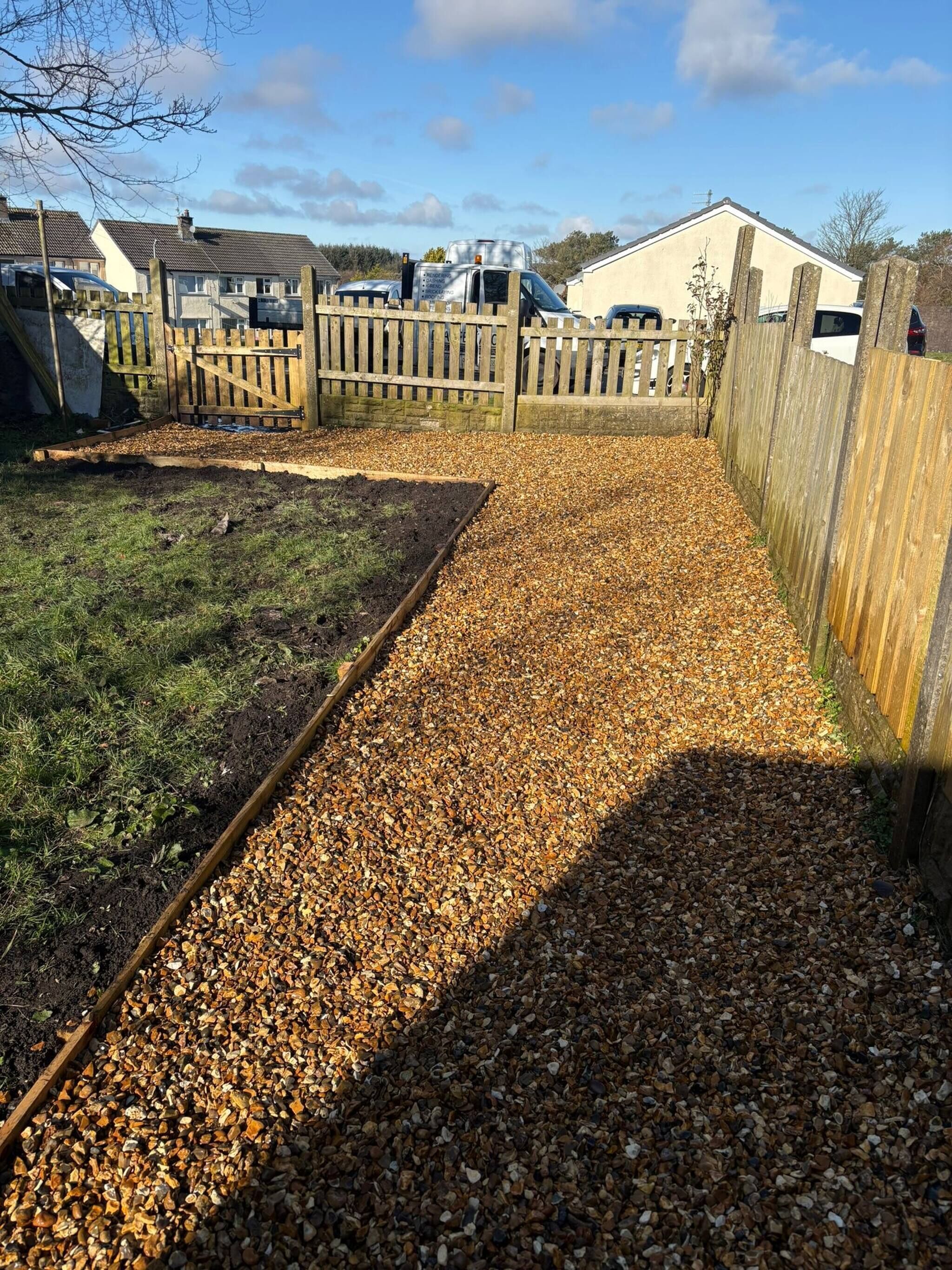 Ein Gartenbereich mit Kiesweg, Holzzaun und kleiner Gartenhütte.