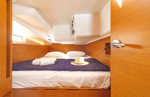 A compact, well-lit room with a bed, pillows, and a hat on the bed.