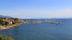 A coastal marina with multiple sailboats docked, a lighthouse, and residential buildings along the shore. - Sun-Kissed Sailing Adventure in the Ionian Islands (Paleros)