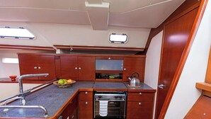 A compact kitchen with wooden cabinets, a built-in oven, and a small window. - Sun-Kissed Sailing Adventure in Islas Sarónicas (Piraeus)