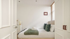 Een slaapkamer met een bed, kussens, een deken, een nachtkastje en een lijstje aan de muur.