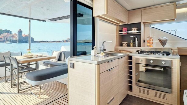 Cocina compacta con estufa, lavamanos y comedor en la cubierta de un barco, con vista al agua.