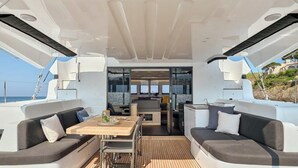 Interior de un yate con comedor, dos sofás, una mesa y vista al mar.