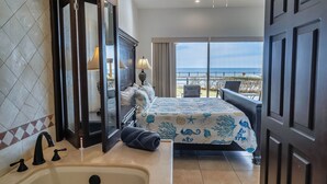 Ein Hotelzimmer mit einem großen Bett, einem Badezimmer mit Waschbecken und Spiegel sowie einem Balkon mit Meerblick.