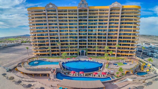 Ein mehrstöckiges Hotel mit Poolbereich, Sitzgelegenheiten im Freien und Blick auf den Strand.