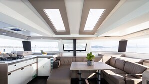 Un intérieur de yacht moderne comprenant une cuisine, un coin salon et de grandes fenêtres offrant une vue sur l’océan.