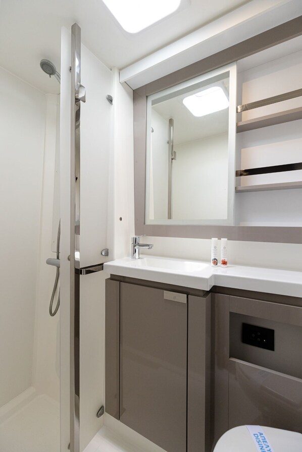 A modern bathroom with a shower, a sink, a mirror, and a toilet. - Sun-Kissed Sailing Adventure in Islas Sarónicas (Alimos)