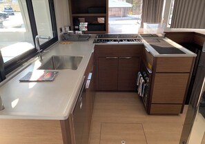 A compact kitchen with a sink, stove, and storage cabinets. - Sun-Kissed Sailing Adventure in Islas Sarónicas (Alimos)