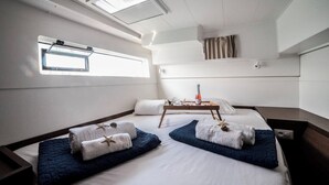 Ett rum med en säng, ett litet bord med en flaska på och ett fönster.