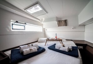 Une pièce avec un lit, une petite table sur laquelle se trouve une bouteille, et une fenêtre.