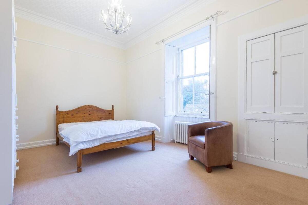 A bedroom with a wooden bed, a radiator, a window, and a wardrobe.