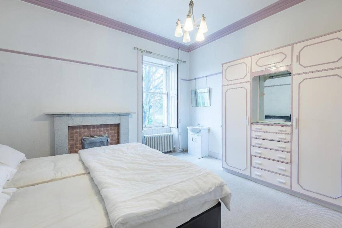 A bedroom with a bed, a fireplace, a window, a wardrobe, and a mirror.