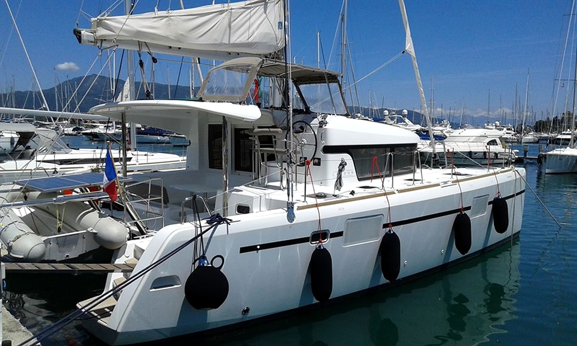 A white yacht docked at a marina with multiple masts, a cabin with windows, and a covered deck area.