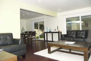 A living room with a dark leather sofa, a wooden coffee table, and a dining area with a glass table and chairs.