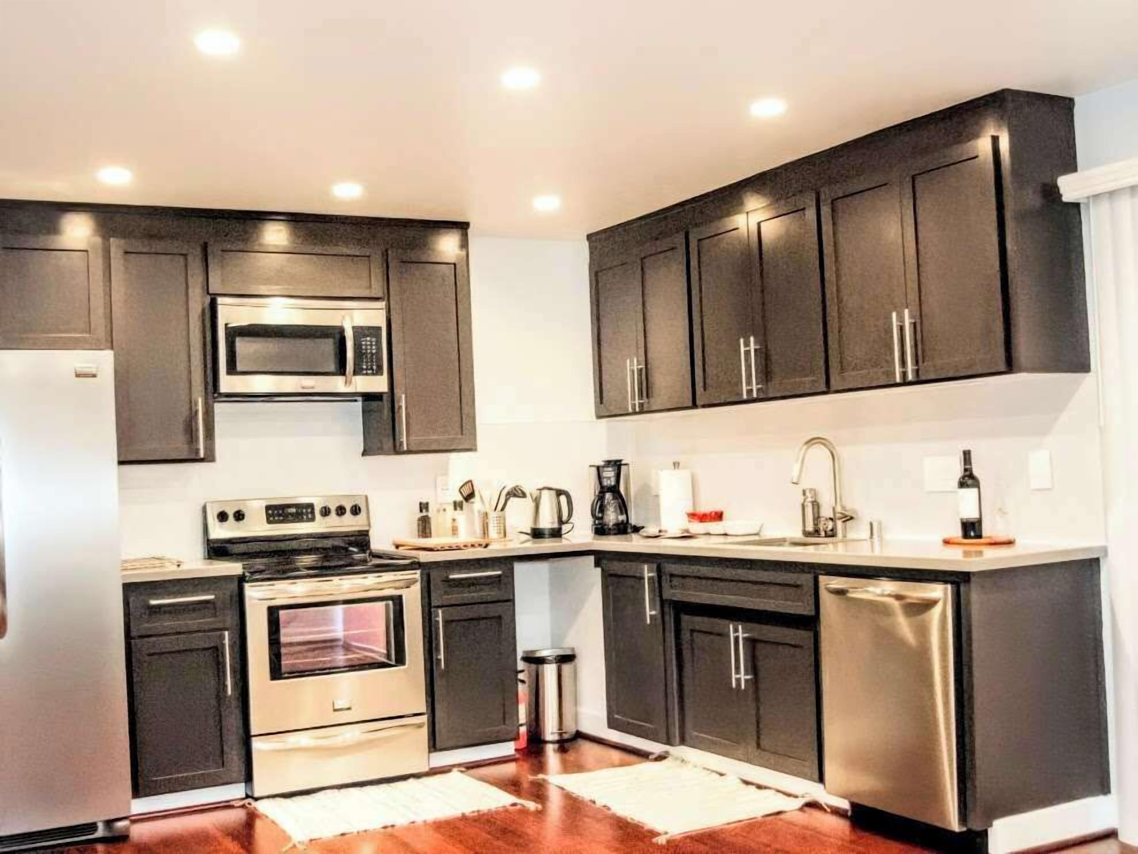 Una cocina moderna con armarios oscuros, electrodomésticos de acero inoxidable y encimera blanca.