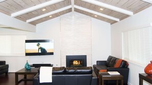 Un soggiorno con camino, televisore e soffitto alto con travi a vista.