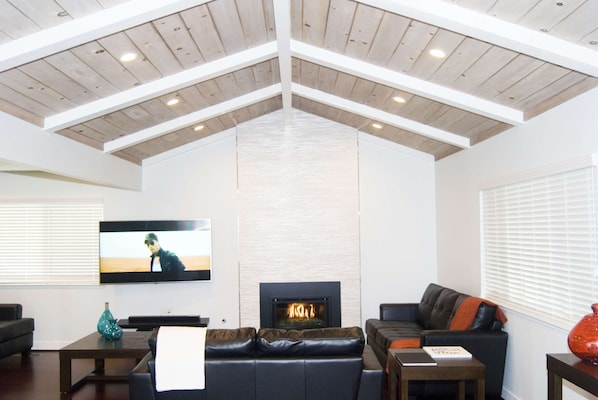 A living room with a fireplace, a television, and a high ceiling with exposed beams.