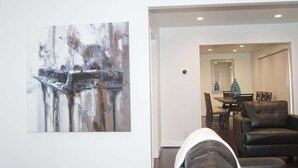 Un interno moderno con un design minimalista, che include una zona pranzo con tavolo e sedie, un divano in pelle nera e un grande quadro astratto appeso al muro.