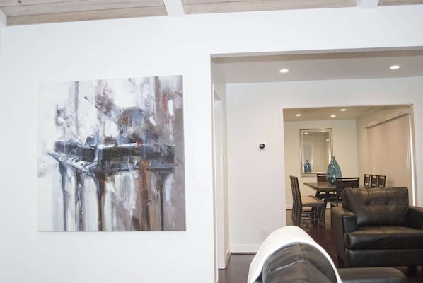 A modern interior with a minimalist design, featuring a dining area with a table and chairs, a black leather sofa, and a large abstract painting on the wall.
