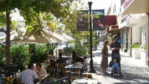 Un caffè all'aperto con tavoli e sedie, immerso nel verde e ombrelloni.