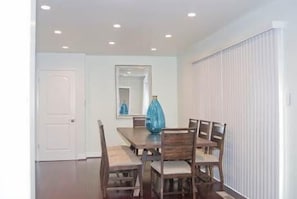 A dining room with a rectangular table, six chairs, a blue vase, a mirror, and a white door.