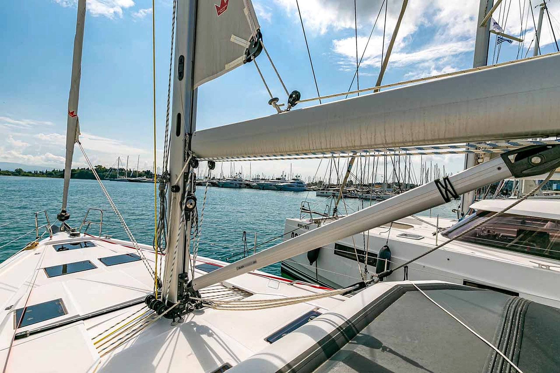 A sailboat with a white hull and multiple sails, docked in a marina with other boats.