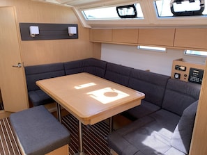 Ein kompaktes Wohnmobil-Interieur mit Holztisch, gepolsterten Sitzen, Bedienfeld und Dachfenster.