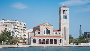 Una iglesia con un campanario alto y un reloj, rodeada de edificios modernos y una orilla de agua.