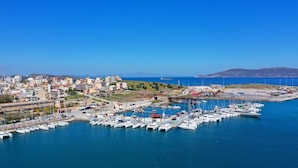 Un port de plaisance où sont amarrés de nombreux bateaux, une ville côtière en arrière-plan et un ciel bleu dégagé.