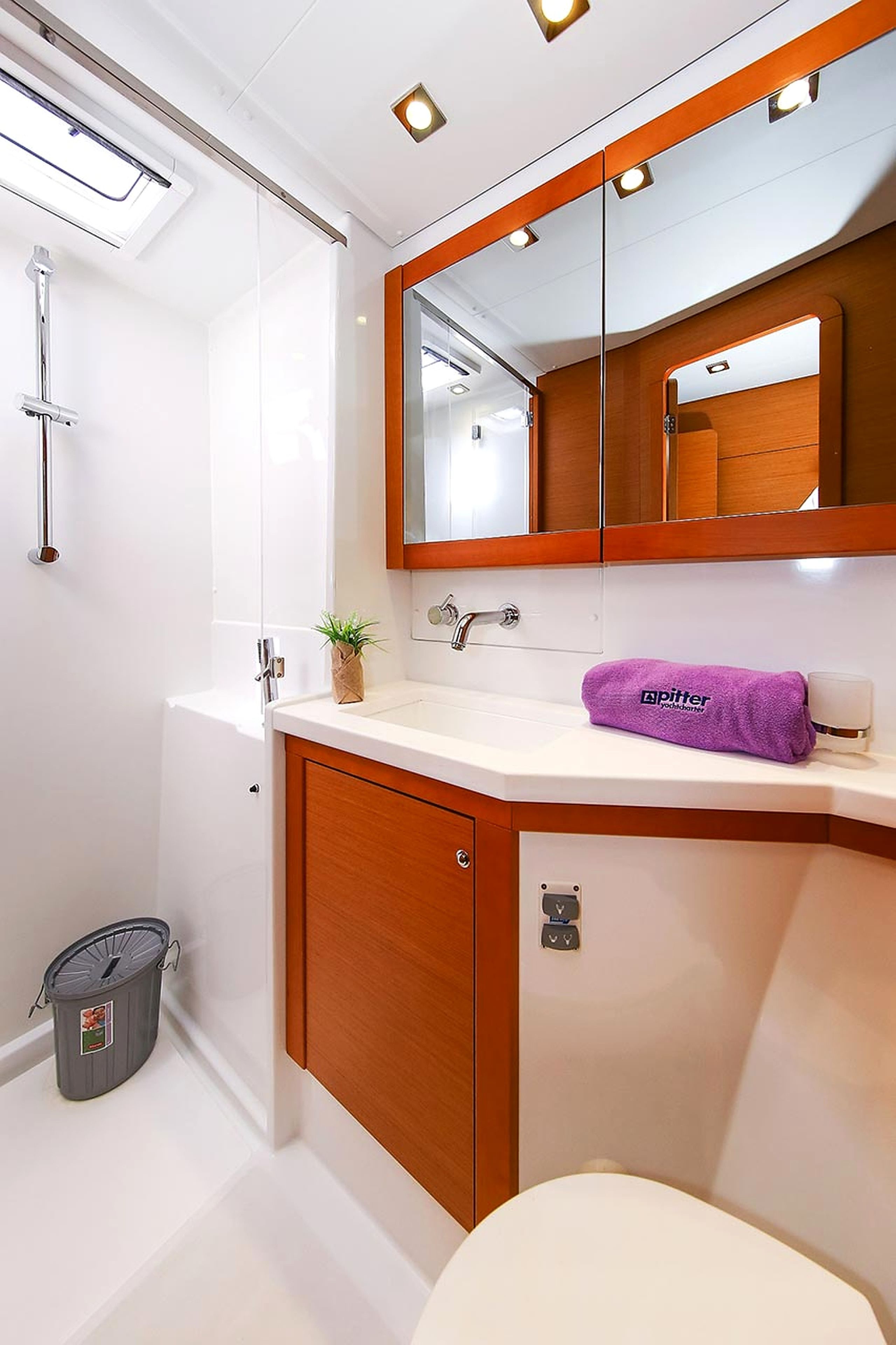 Un baño con lavamanos blanco, tocador de madera, espejo, toalla y zona de ducha.