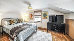 A bedroom with a bed, bedside table, lamp, artwork, television, and a wardrobe.