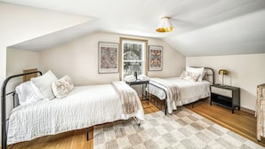 A bedroom with two beds, a window, a lamp, and artwork on the walls.