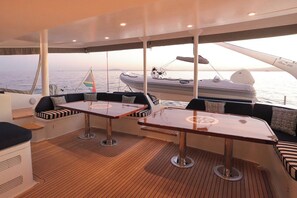Ein Yachthausdeck mit Sitzbereichen, Tischen und Blick auf das Meer.