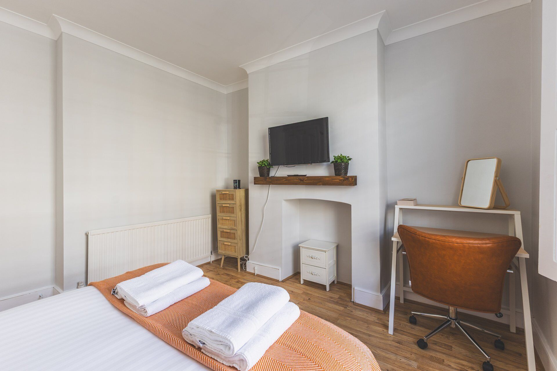 Una camera d'hotel con un letto, una scrivania con una sedia, una televisione, un caminetto e uno specchio.