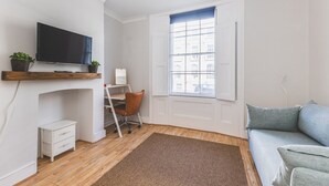 Quarto com televisão, escrivaninha, cadeira, sofá e janela.