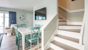 A modern interior with a dining area, staircase, and a flat-screen TV mounted on the wall. - The Scallop (Carolina Beach)