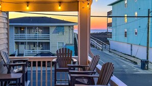 A balcony with chairs and a table, overlooking a street with buildings and a sunset. - The Scallop (Carolina Beach)