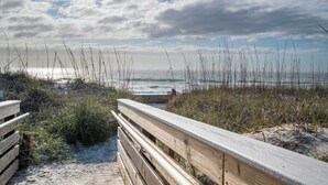 A wooden boardwalk leading to a beach with overcast skies. - The Scallop (Carolina Beach)