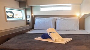 Cabine compacta e bem iluminada com cama, almofadas, uma mesinha e um painel de controle.