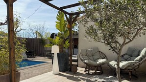 Eine Holzterrasse mit Pool, zwei Korbstühle, einem Blumentopf und einer weißen Lampe.