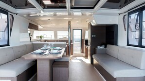A modern interior with a central dining table, cushioned seating, and a view through an open door. - Sun-Kissed Sailing Adventure in the Dodecanese Islands (Kos)