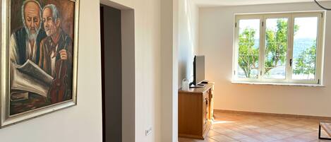 A room with a large window, a painting on the wall, and a desk with a computer.