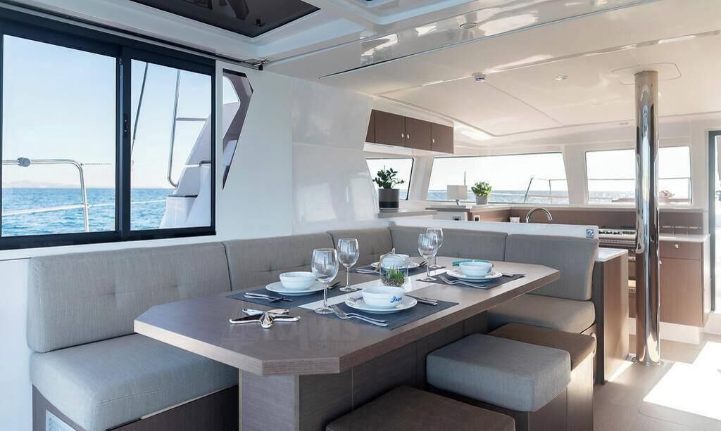 A modern yacht interior with a dining area, seating, and a view of the sea.