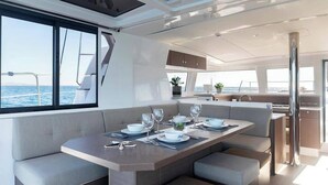 A modern yacht interior with a dining area, seating, and a view of the sea. - Sun-Kissed Sailing Adventure in Islas Sarónicas (Alimos)