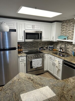 A modern kitchen with white cabinets, stainless steel appliances, granite countertops, and a backsplash with a mosaic tile pattern. - Beach Condo 2 Bed / 2 Bath Right Next Door to the Famous Flora-Bama -Phoenix X (Orange Beach)