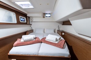 Un lit double avec des serviettes blanches et roses, une petite fenêtre et un ventilateur.