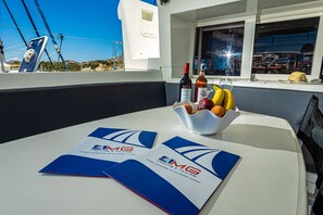 Une table avec des brochures, une bouteille de vin et un panier de fruits sur le pont d’un bateau.