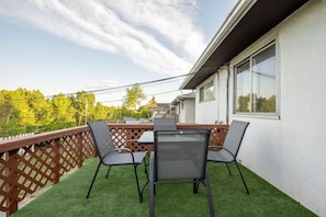 A balcony with a table and chairs, a wooden fence, and a view of trees and buildings.