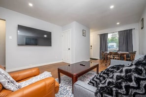 Ein Wohnzimmer mit Fernseher, einer Ledersofa, einem Couchtisch und einem Essbereich mit Stühlen und einem Tisch.