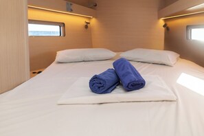 A bed with white linens, two rolled blue towels, and a window on the wall. - Sun-Kissed Sailing Adventure in Islas Sarónicas (Alimos)